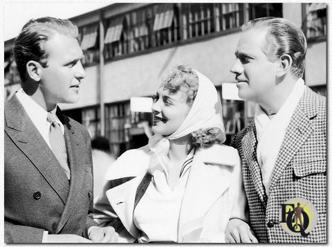 Reunion at Columbia! Melvyn Douglas (R), escorting Virginia Bruce, his leading lady in Columbia's "Women of Glamour" to the set, encounters Ralph Bellamy, long-time friend. Ten years ago Douglas and Bellamy were competing stock company impresarios. Today they are both under long-term contract to Columbia.(ca. Feb 1937)