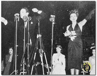 Paulette Goddard veilt haar orchideeëncorsage met William Gargan die de biedingen leidt tijdens de War Bond Rally in Madison Square Garden (september 1942).