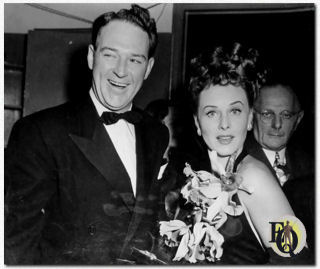 Paulette Goddard veilt haar orchideeëncorsage met William Gargan die de biedingen leidt tijdens de War Bond Rally in Madison Square Garden (30 september 1942).