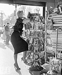 Kim Novak posing in front of a book stand with the Pocket Book edition for Ellery Queen's "The Virgin Heiresses" (1954) in the middle (third from the bottom). Click for the larger version.