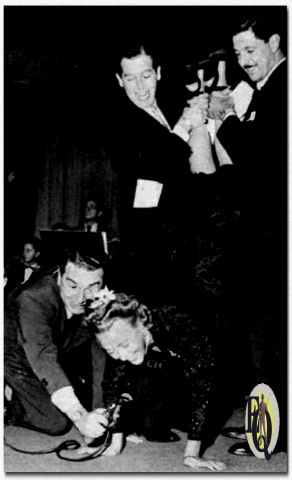 "Let Yourself Go" that zany, exhibitionistic program which couldn't fit comedian -emcee Milton Berle more perfectly if it were tailored for him. DIVA GRACE MOORE gets in the spirit by singing upside-down, aided by scripter Hal Block, supported by Milton Berle and announcer Ken Roberts.